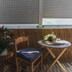 Przytulna loggia w bloku z drewnianym krzesłem, stolikiem i roślinami. Idealne miejsce na poranną kawę.