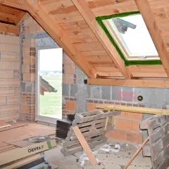 Wnętrze domu w budowie, widoczne połaciowe okno dachowe i ściany z pustaków.