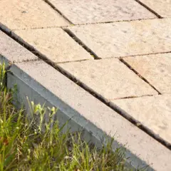 Obrzeża trawnikowe z kostki betonowej oddzielają zieloną trawę od ścieżki z płyt.