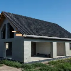 Dom w stanie surowym otwartym, z dachem pokrytym czarną dachówką. Widać otwory okienne i drzwiowe. Idealny moment na ustalenie ceny za m2 robocizny.