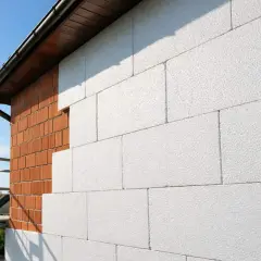 Ściana domu w trakcie ocieplania. Widoczna cegła i biały styropian.