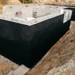 Solidny fundament domu w budowie, z czarną izolacją przeciwwilgociową.