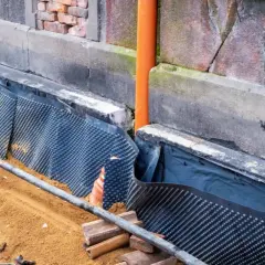 Prace przy izolacji fundamentów w starym domu. Widoczna membrana kubełkowa i rura odpływowa.