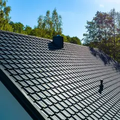 Nowoczesny dach pokryty ciemną blachodachówką, z kominem i anteną. Wybór między dachówką a blachodachówką jest ważny.