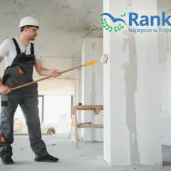 Remontujący mężczyzna w kasku maluje ścianę wałkiem.