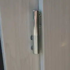 Metalowy zawias na jasnych drzwiach, umożliwiający regulację ich położenia.