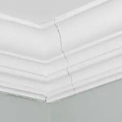 Pęknięcie na białym suficie, widoczne na styku ścian i ozdobnej listwy.