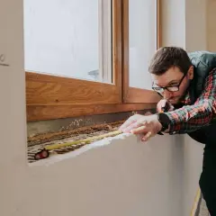 Mężczyzna mierzy parapet pod drewnianym oknem, planując jakie okna do domu będą najlepsze.