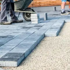 Układanie podjazdu z betonu szczotkowanego. Pracownicy układają kostkę brukową na podsypce.