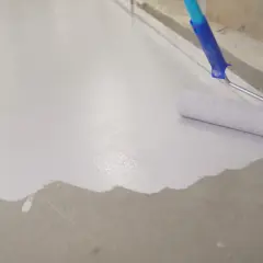 Wałek maluje beton na biało, tworząc gładką, jednolitą powierzchnię.