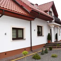 Eleganckie wykończenie dołu elewacji domu z brązowymi rynnami i ozdobnymi kamieniami wokół.