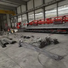 Stal zbrojeniowa w magazynie, gotowa do użycia w budowie. W tle maszyna do produkcji elementów betonowych.