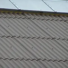 Faliste pokrycie dachu z płyty eurofala, szare, z widocznymi punktami mocowania. Nad nim błyszczący dach.