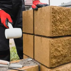 Budowa ogrodzenia z bloczków fundamentowych. Rękawice ochronne i gumowy młotek pomagają układać kolejne elementy.