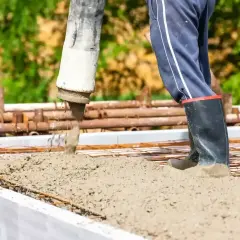 Beton wylewany jest na zbrojenie w szalunku. Pracownik w gumowcach stoi w świeżym betonie.