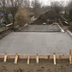 Plac budowy z wylana płytą fundamentową, przygotowaną pod klasę ekspozycji betonu. Widać zbrojenie i szalunki.