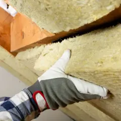 Ręka w rękawicy układa wełnę mineralną na poddaszu. To dobry wybór, jaka wełna na poddasze, by ocieplić dom.