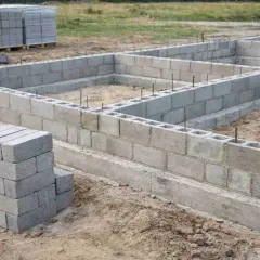 Budowa fundamentów z bloczków betonowych. Stos pustaków betonowych obok wznoszonej ściany.
