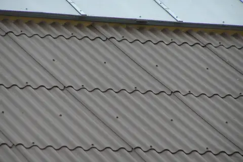 Faliste pokrycie dachu z płyty eurofala, szare, z widocznymi punktami mocowania. Nad nim błyszczący dach.