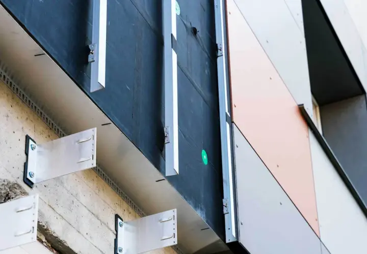 System mocowania elewacji wentylowanej. Metalowe wsporniki przytwierdzone do betonowej ściany, tworzące przestrzeń wentylacyjną pod panelami.