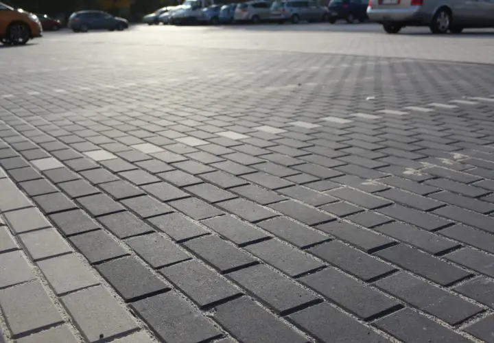 Szary parking wyłożony kostką brukową holland. W tle widać zaparkowane samochody.