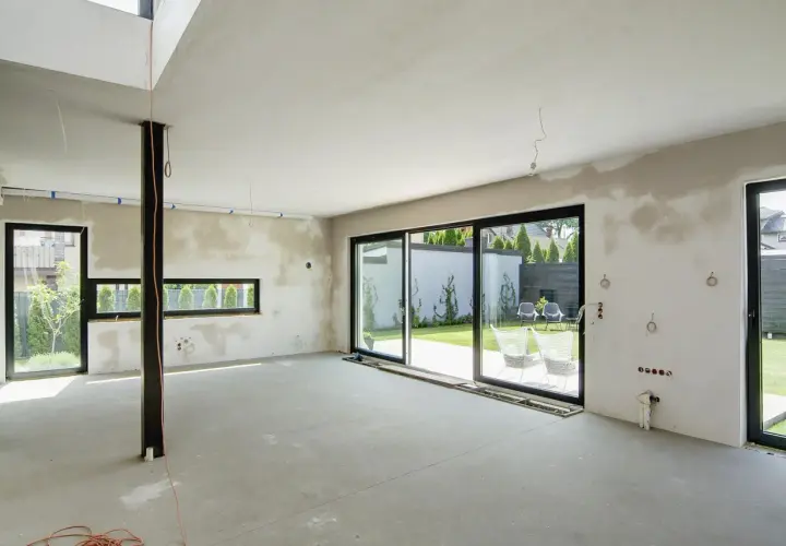 Wnętrze domu w budowie, przygotowane do tynkowania. Duże okna wychodzą na ogród. Szacowany koszt tynkowania domu 120m2.