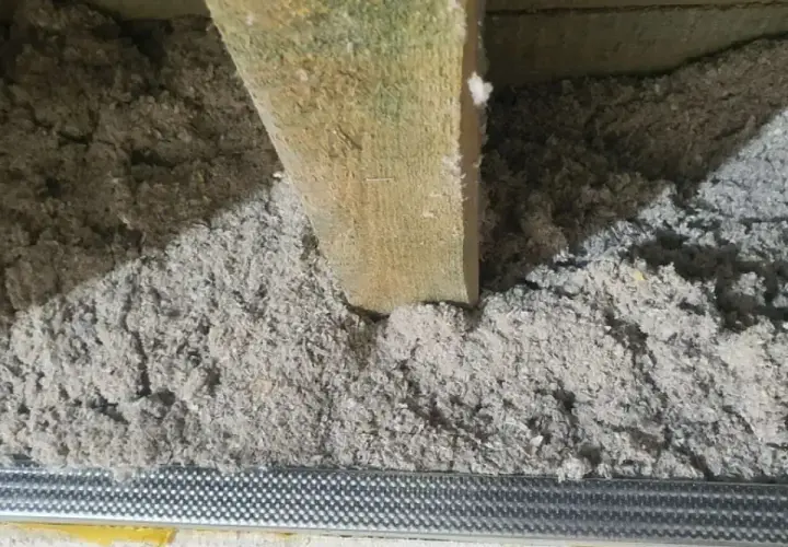 Drewniana belka w luźnej, szarej masie. To celuloza ocieplenie, które zapewnia komfort termiczny.