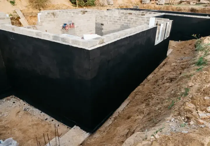 Solidny fundament domu w budowie, z czarną izolacją przeciwwilgociową.