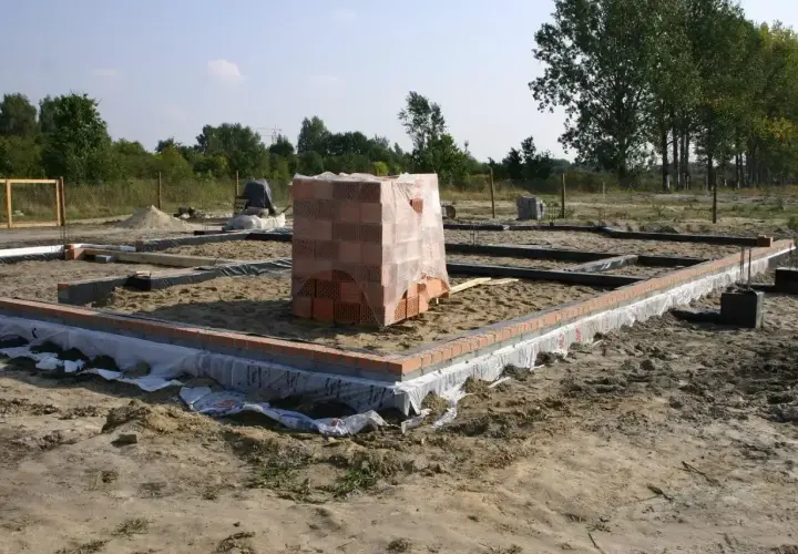 Rozpoczęcie budowy domu: wykopy pod fundamenty, ułożone bloczki i paleta cegieł.