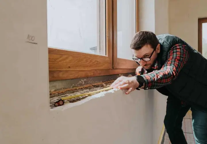 Mężczyzna mierzy parapet pod drewnianym oknem, planując jakie okna do domu będą najlepsze.