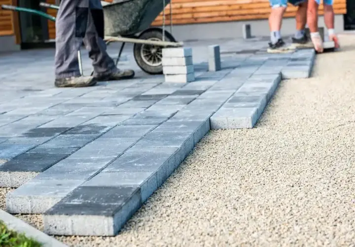 Układanie podjazdu z betonu szczotkowanego. Pracownicy układają kostkę brukową na podsypce.