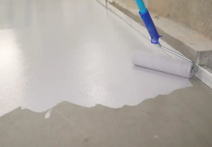 Wałek maluje beton na biało, tworząc gładką, jednolitą powierzchnię.