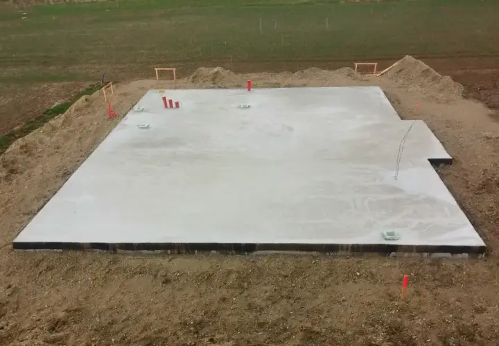 Płyta fundamentowa koszt. Betonowa płyta na budowie, otoczona ziemią i materiałami budowlanymi.