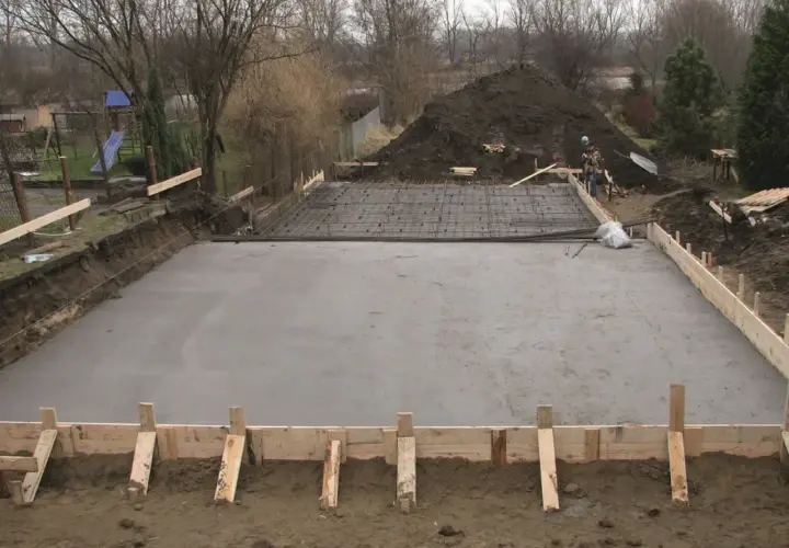 Plac budowy z wylana płytą fundamentową, przygotowaną pod klasę ekspozycji betonu. Widać zbrojenie i szalunki.