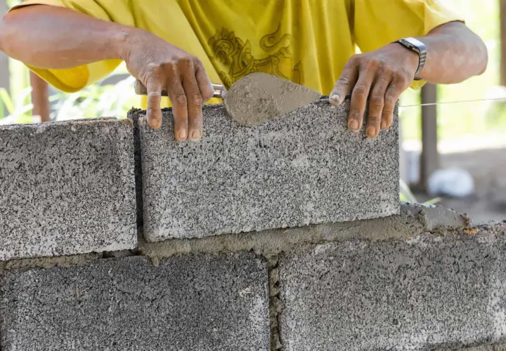 Murarz układa bloczek betonowy, sprawdzając jego wymiary.