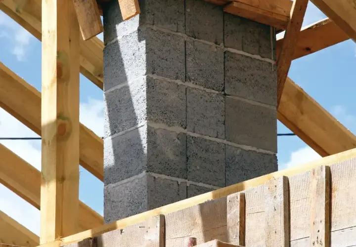 Budowa komina systemowego z bloczków betonowych, widoczny fundament i drewniana konstrukcja dachu.