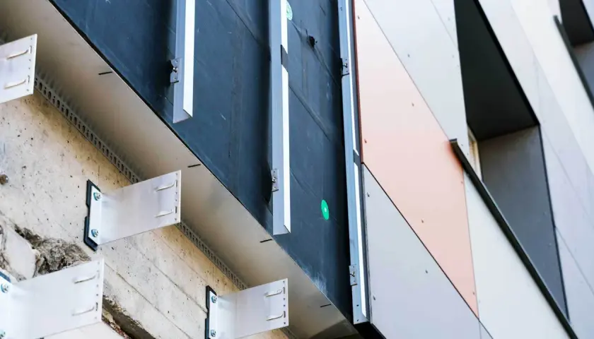 System mocowania elewacji wentylowanej. Metalowe wsporniki przytwierdzone do betonowej ściany, tworzące przestrzeń wentylacyjną pod panelami.