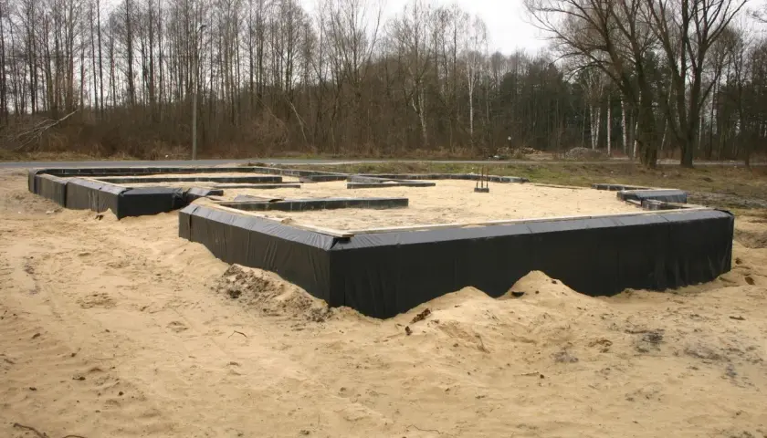 Izolacja starych fundamentów z kamienia w trakcie budowy. Czarna folia zabezpiecza ściany przed wilgocią.