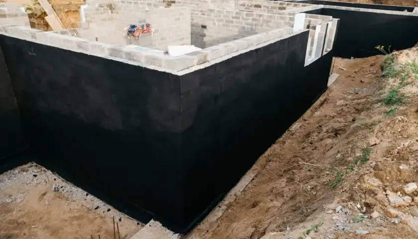 Solidny fundament domu w budowie, z czarną izolacją przeciwwilgociową.
