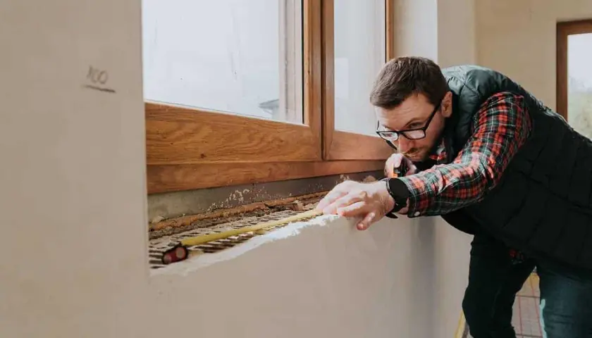 Mężczyzna mierzy parapet pod drewnianym oknem, planując jakie okna do domu będą najlepsze.