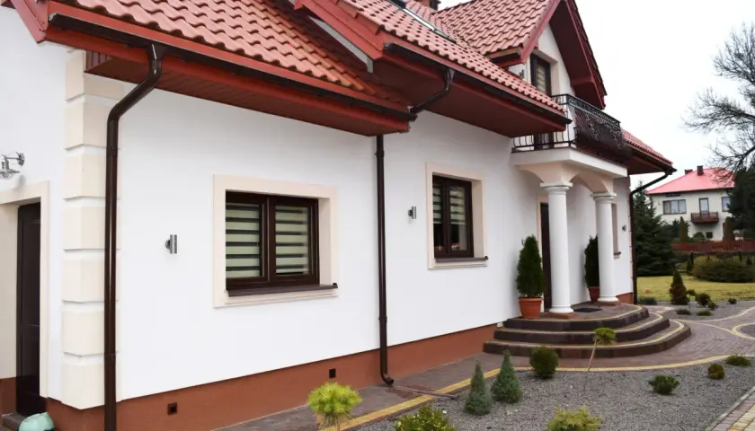 Eleganckie wykończenie dołu elewacji domu z brązowymi rynnami i ozdobnymi kamieniami wokół.