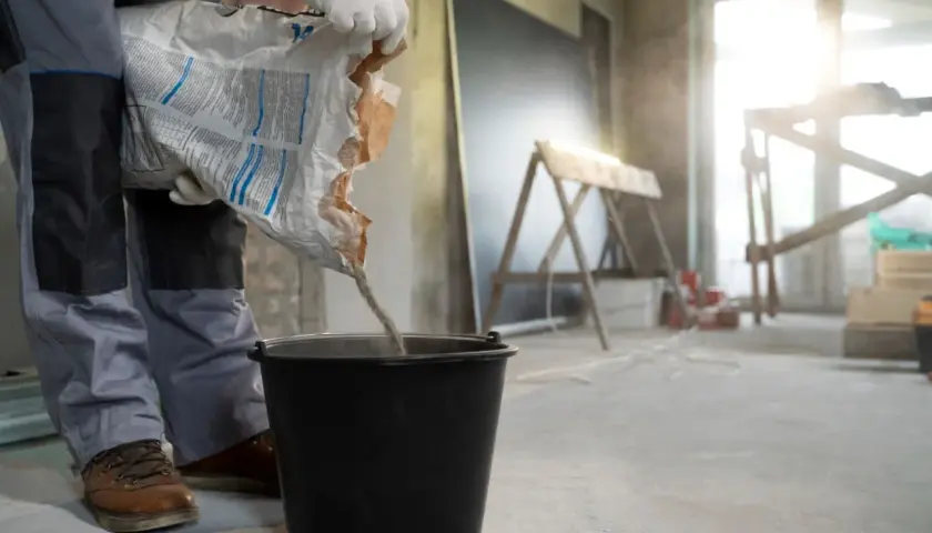 Budowlaniec wsypuje mieszankę do wiadra, przygotowując beton na styropianie. Kluczowa jest minimalna grubość wylewki betonowej na styropianie.