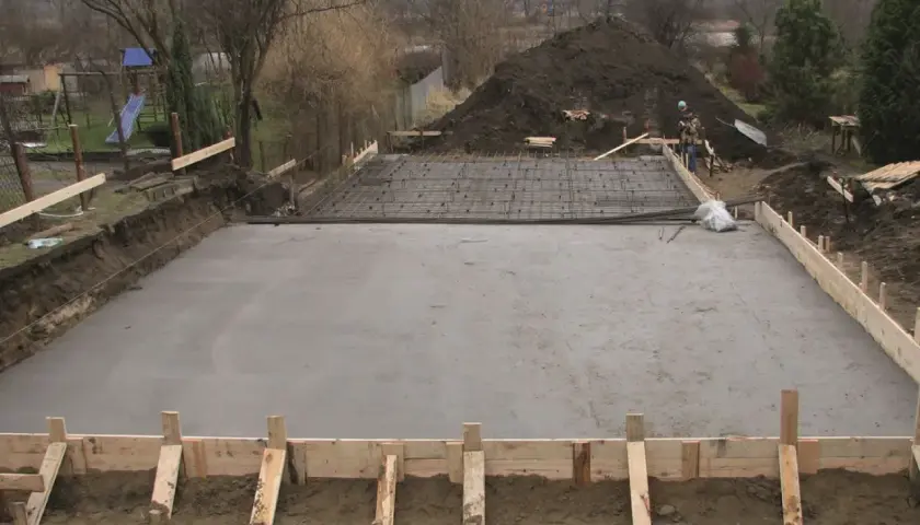 Plac budowy z wylana płytą fundamentową, przygotowaną pod klasę ekspozycji betonu. Widać zbrojenie i szalunki.