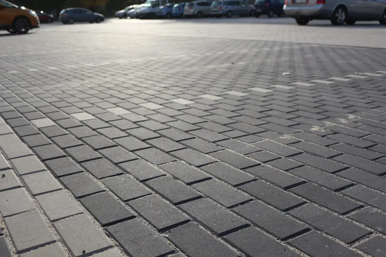 Szary parking wyłożony kostką brukową holland. W tle widać zaparkowane samochody.