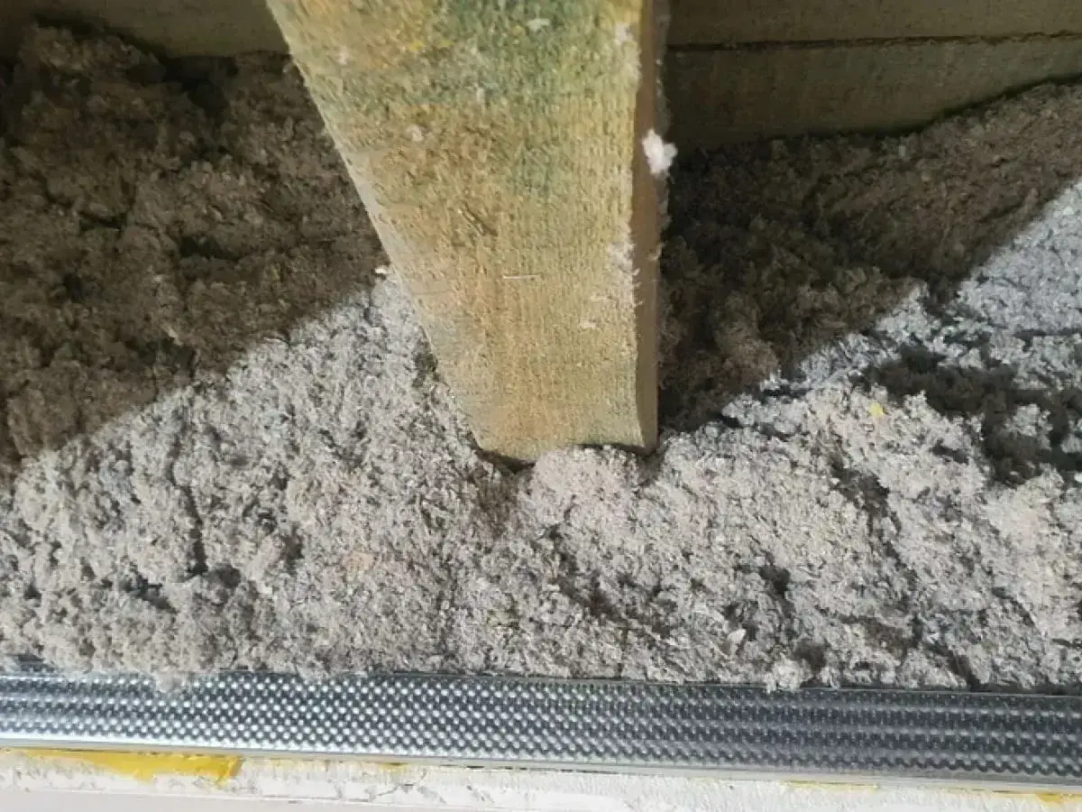 Drewniana belka w luźnej, szarej masie. To celuloza ocieplenie, które zapewnia komfort termiczny.
