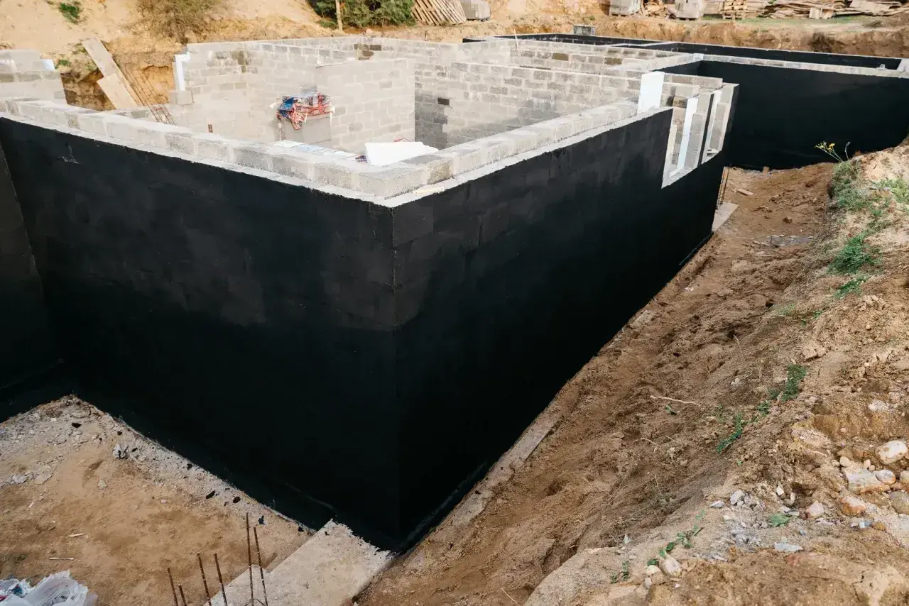 Solidny fundament domu w budowie, z czarną izolacją przeciwwilgociową.