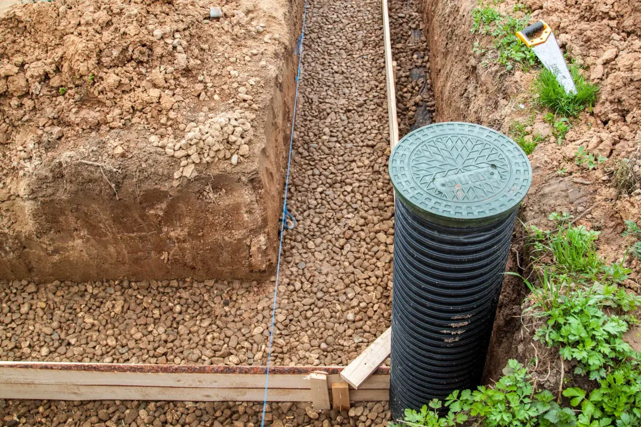 Budowa odwodnienia domu: wykop, rura drenarska, kruszywo i studzienka rewizyjna.
