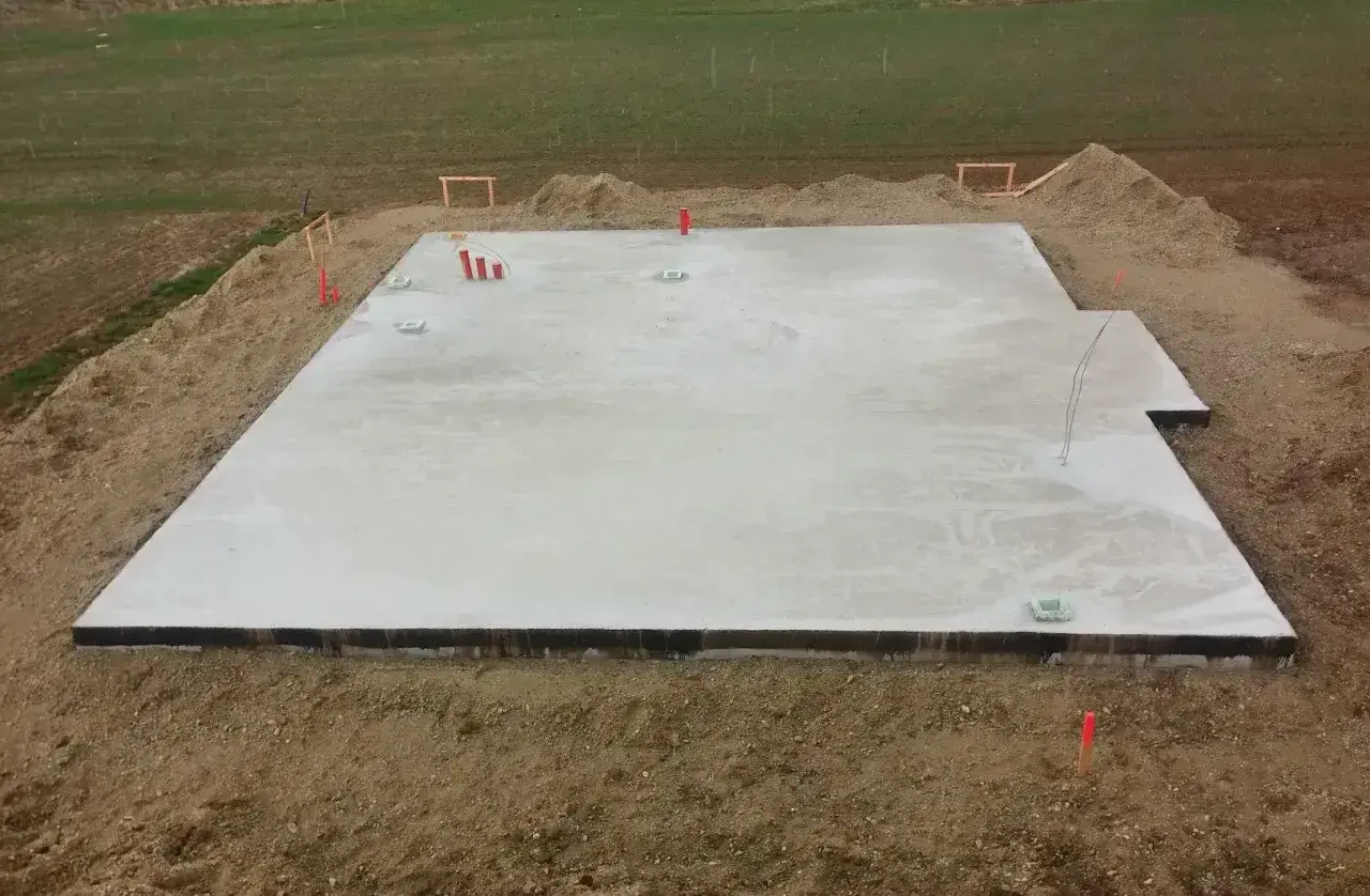 Płyta fundamentowa koszt. Betonowa płyta na budowie, otoczona ziemią i materiałami budowlanymi.