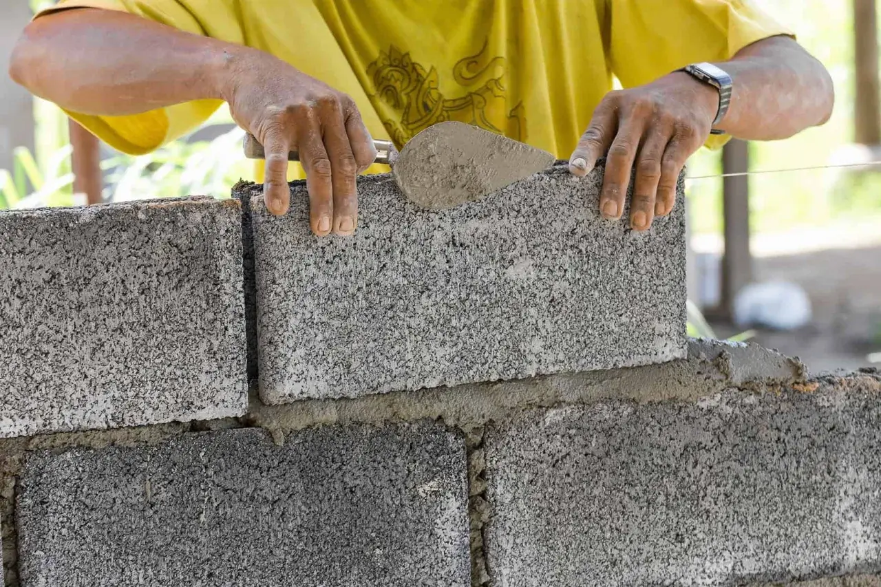 Murarz układa bloczek betonowy, sprawdzając jego wymiary.