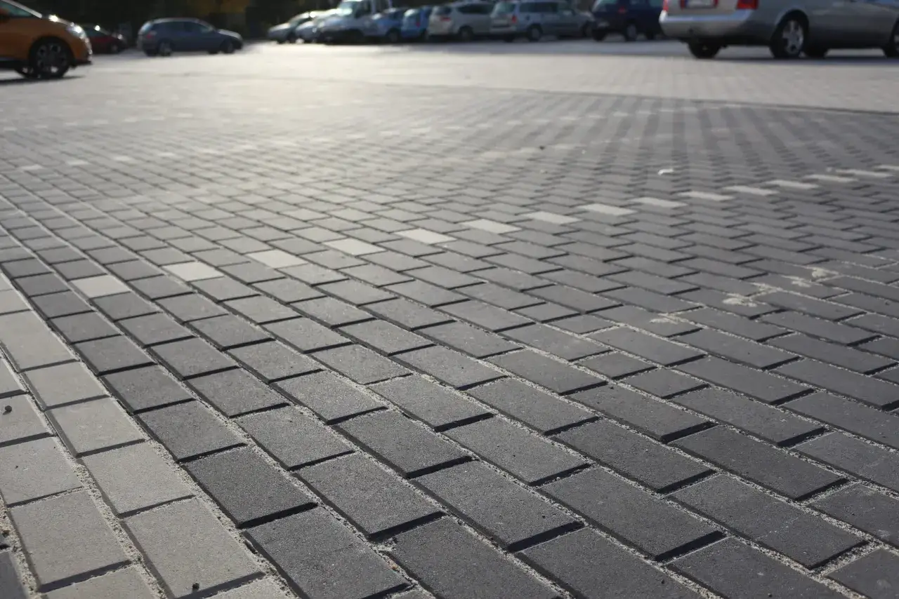 Szary parking wyłożony kostką brukową holland. W tle widać zaparkowane samochody.